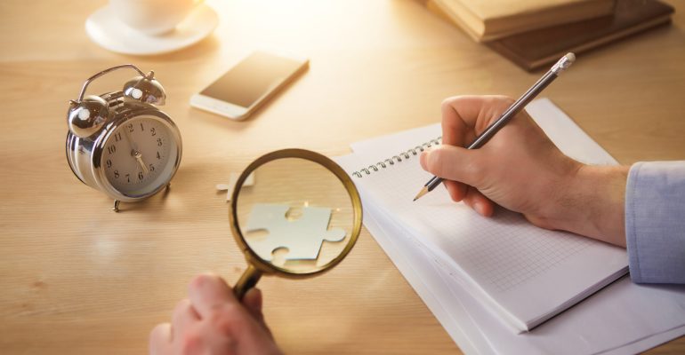 The male hands with a pencil and magnifying glass